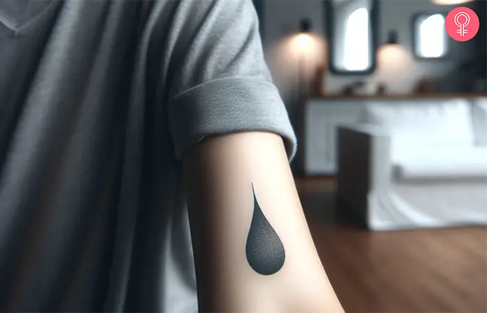 Eine Frau mit einem minimalistischen schwarzen Wassertropfen-Tattoo auf dem Arm