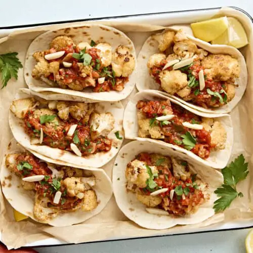 Draufsicht auf Blumenkohl-Tacos mit Romesco-Sauce in einer mit Backpapier ausgelegten Auflaufform