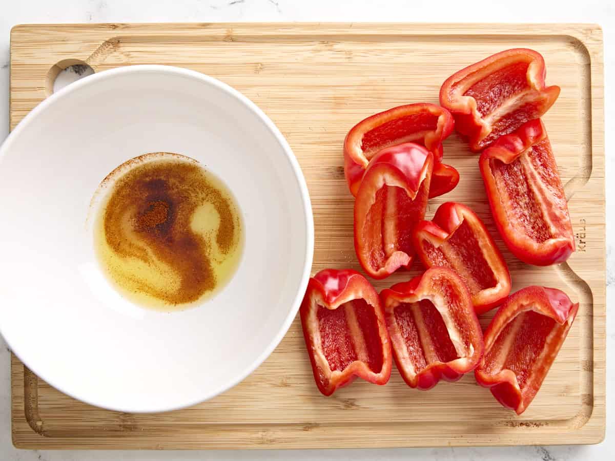 Geviertelte und entkernte rote Paprika neben einer Schüssel mit Gewürzen