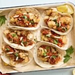 Overhead view of cauliflower tacos with romesco sauce in a parchment lined baking dish