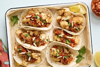 Overhead view of cauliflower tacos with romesco sauce in a parchment lined baking dish