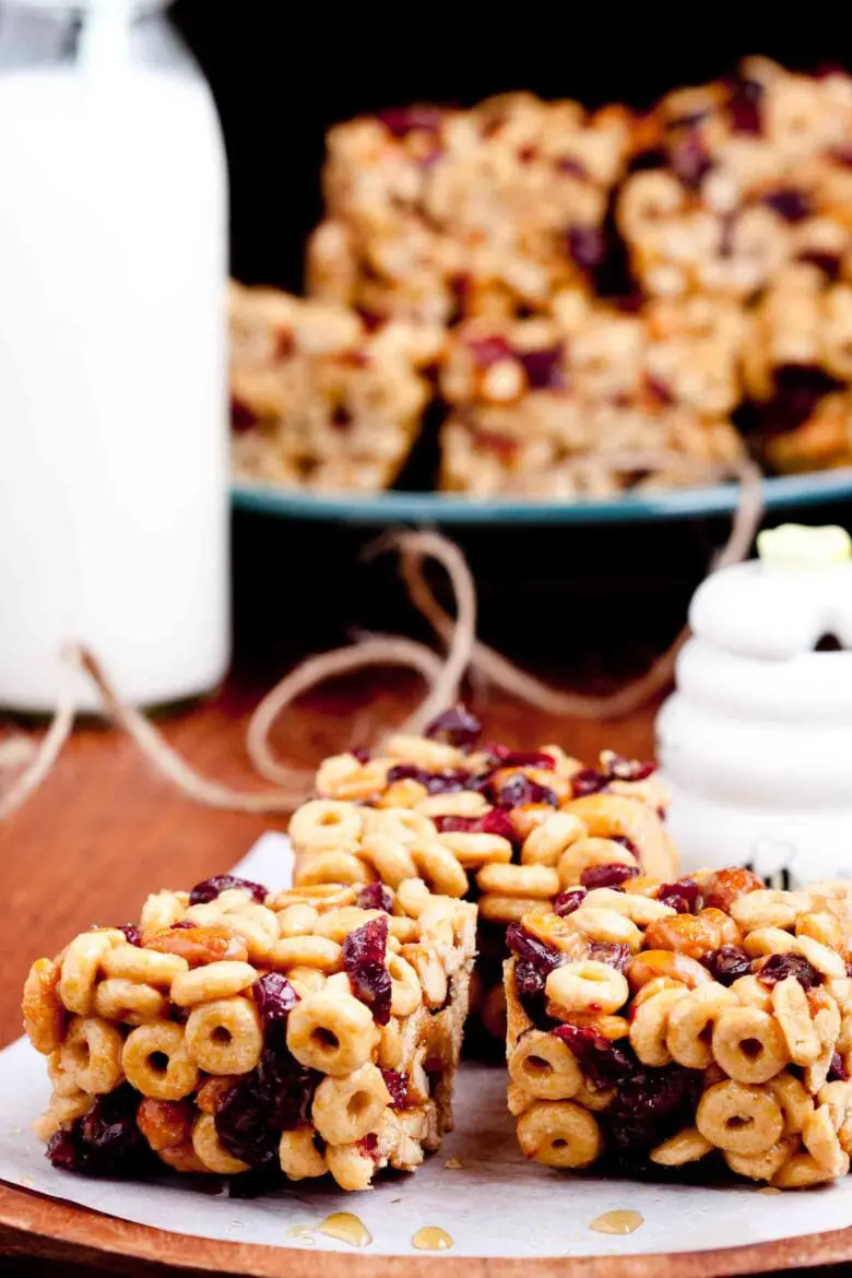 Eine Nahaufnahme von drei Erdnussbutter-Cheerios-Riegeln mit sichtbaren Cheerios und Trockenfrüchten, auf Pergamentpapier platziert. 