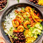 shrimp bowls plated in black bowls with a gold fork with shrimp and bell peppers on top of white rice