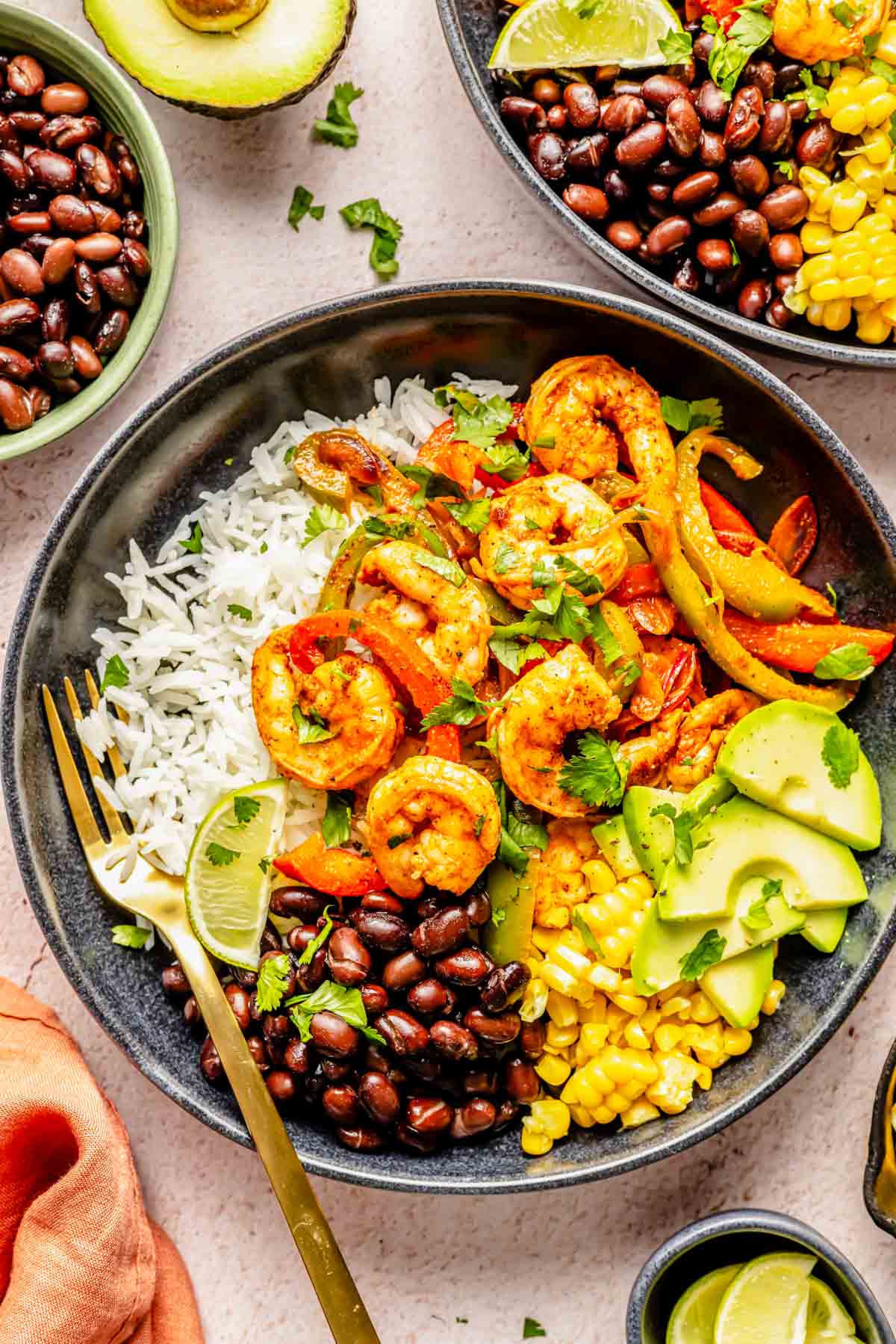 shrimp bowls plated in black bowls with a gold fork with shrimp and bell peppers on top of white rice