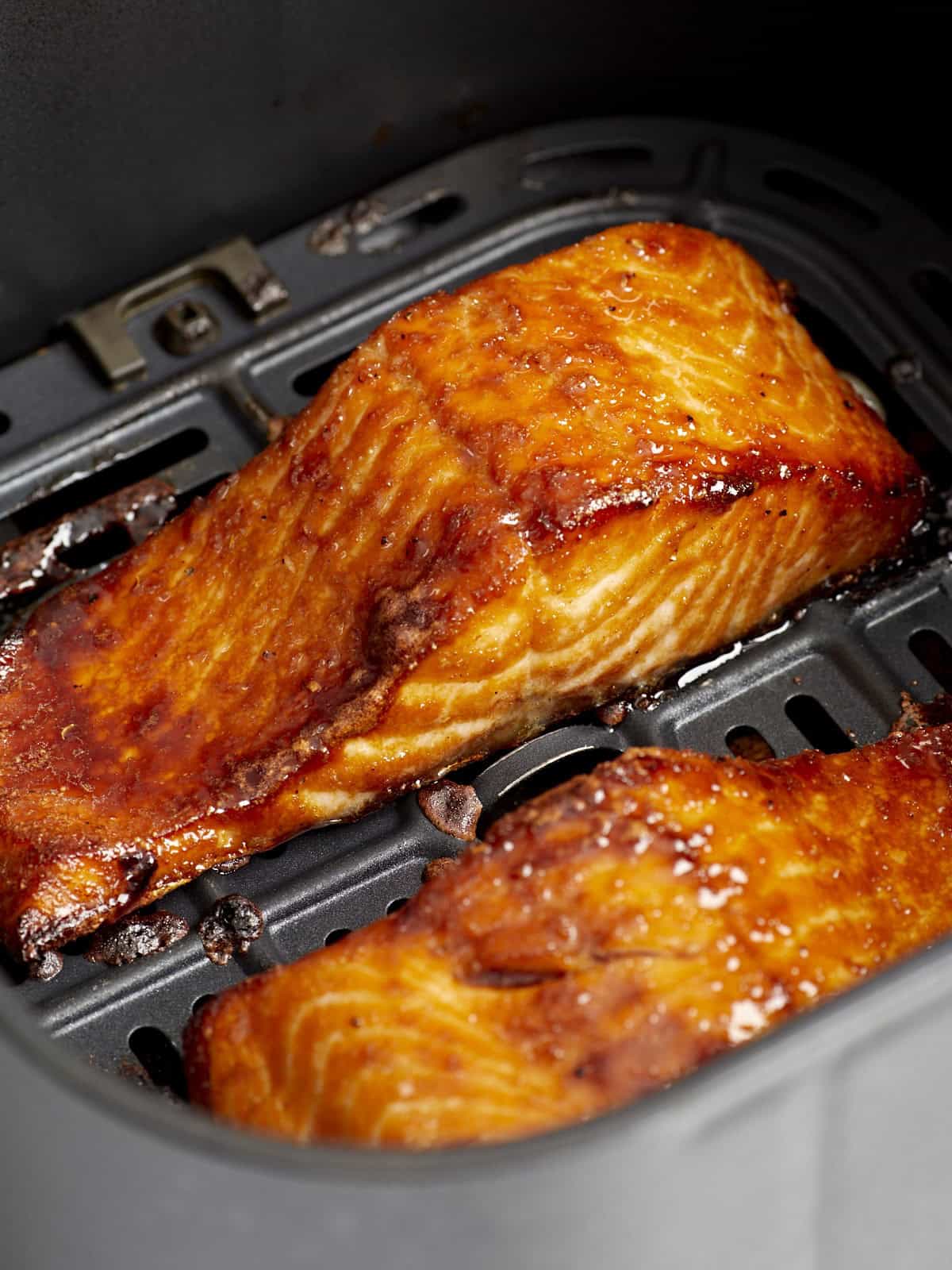 Nahaufnahme von Lachsfilets in einem Frittierkorb aus der Heißluftfritteuse.