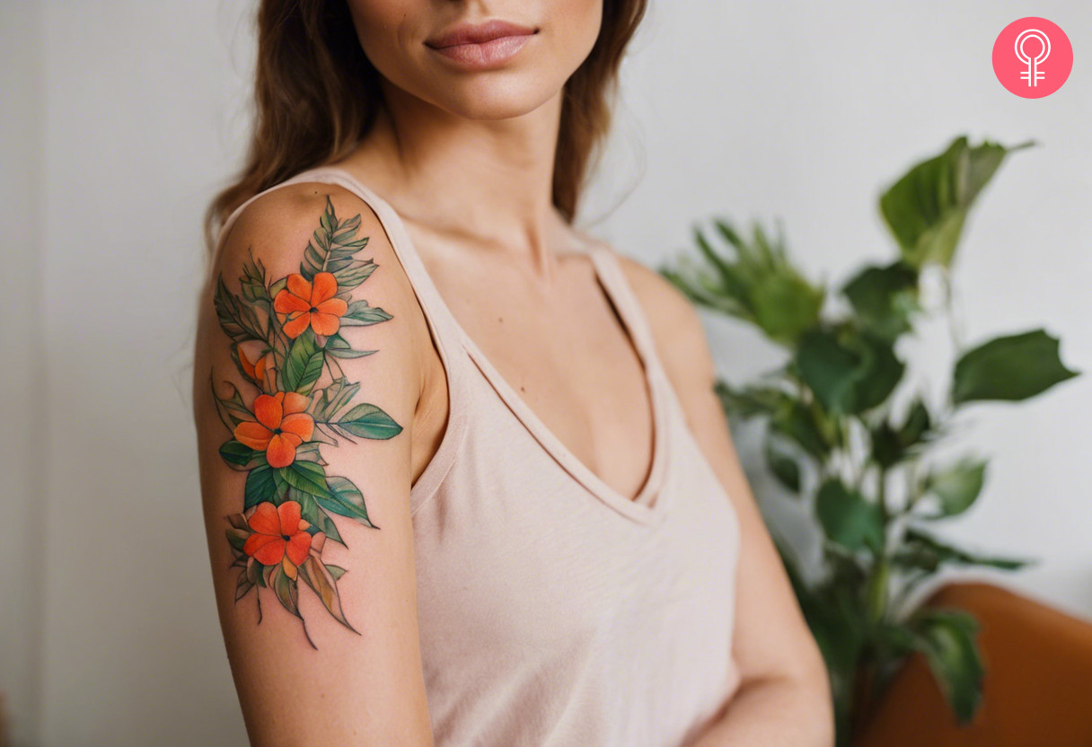 Ein lebendiges Laubtattoo mit kleinen orangefarbenen Blumen auf dem Oberarm einer Frau