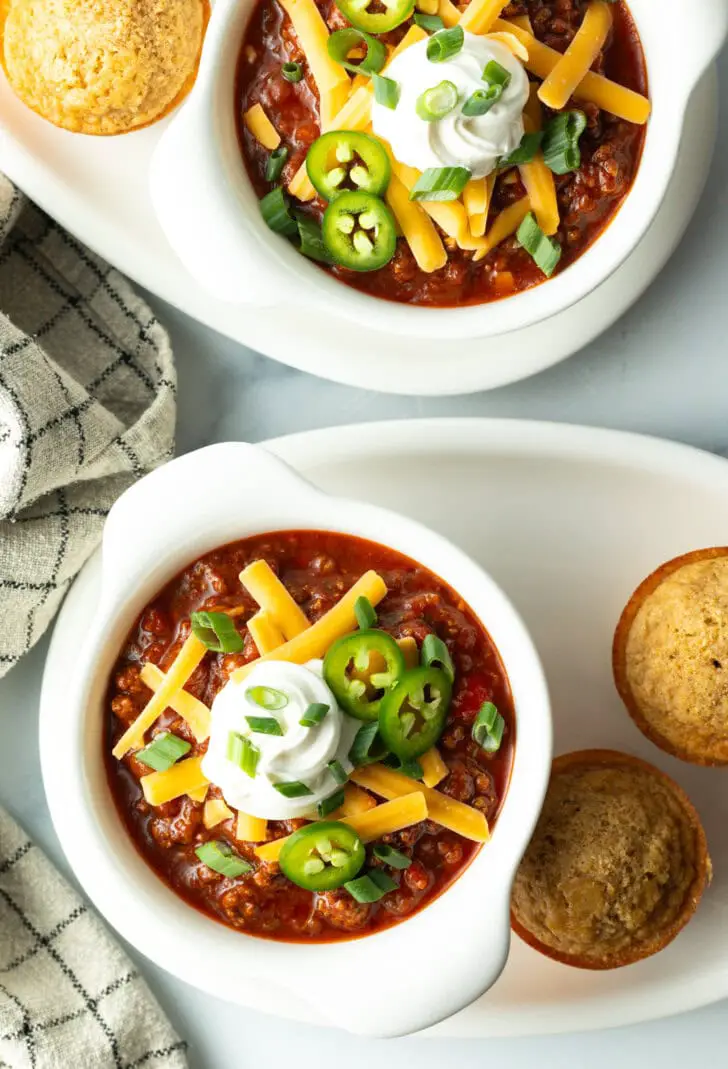 Draufsicht auf eine weiße Schüssel Chili con Carne ohne Bohnen, garniert mit geriebenem Käse, Jalapeño-Scheiben, Sauerrahm und gehackten Frühlingszwiebeln.