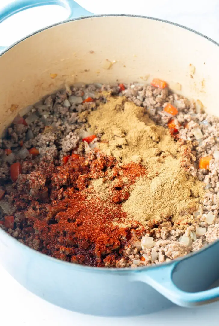 Gekochtes Hackfleisch und Gewürze in einem großen blauen Kochtopf.