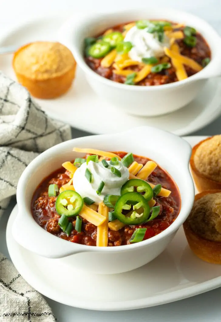 Draufsicht auf eine weiße Schüssel Chili con Carne ohne Bohnen, garniert mit geriebenem Käse, Jalapeño-Scheiben, Sauerrahm und gehackten Frühlingszwiebeln.