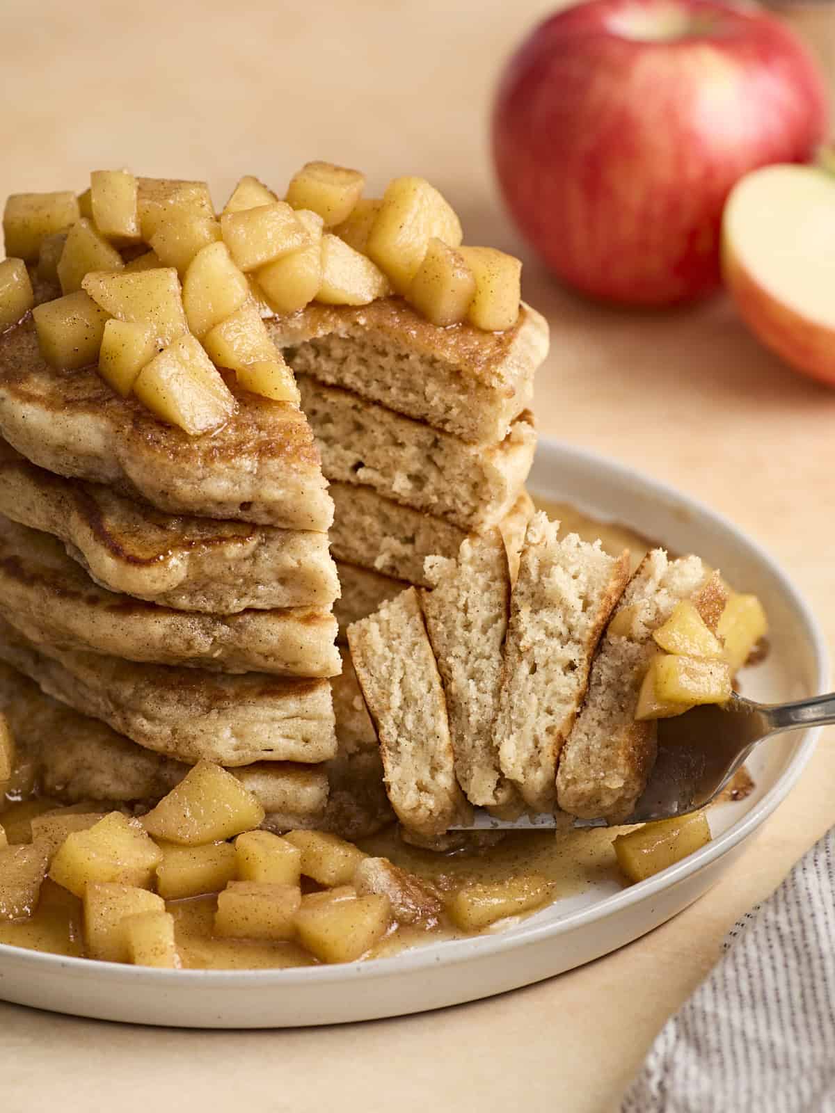 Vorderansicht eines Stapels Apfel-Zimt-Pfannkuchen, aus dem einige mit der Gabel herausgehoben wurden.