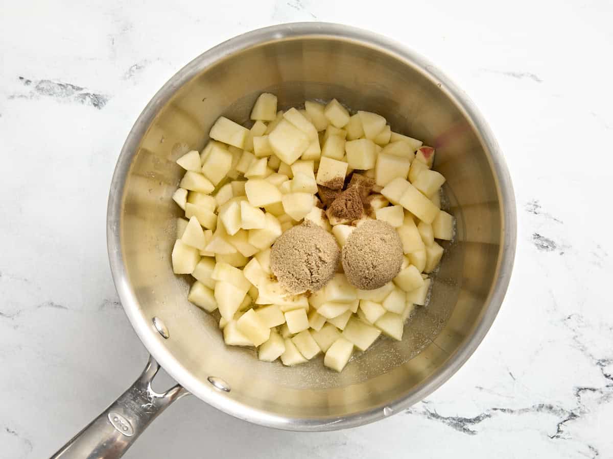 Gehackte Äpfel, brauner Zucker und Zimt in einem kleinen Topf.