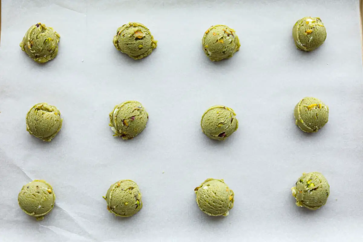 Overhead shot of cookie dough scooped into balls spread out on a cookie sheet covered in parchment paper. 