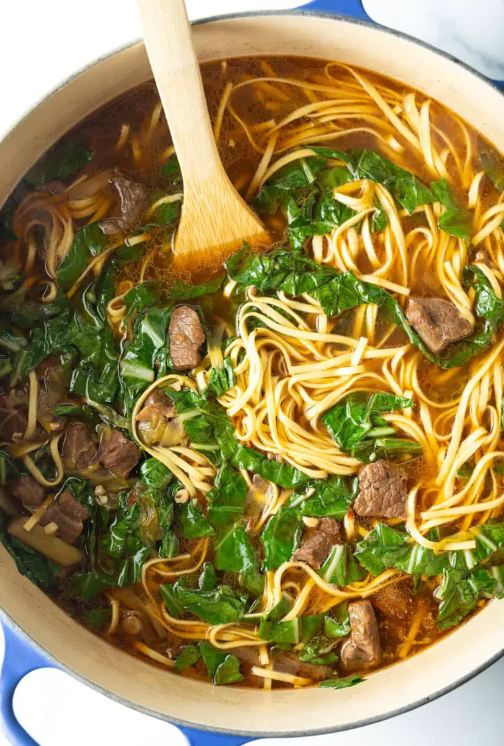 Von oben gesehen ein großer Topf Suppe mit Nudeln und Gemüse, umgerührt mit einem Holzspatel.