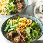 Bowl of Taiwanese beef soup with noodles, green scallions, and chopped bok choy.