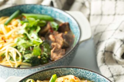 Bowl of Taiwanese beef soup with noodles, green scallions, and chopped bok choy.