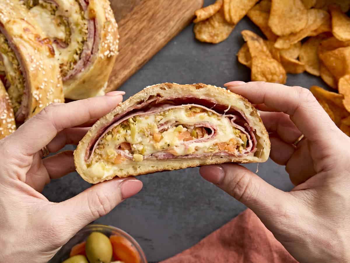 Hände halten ein Stück Muffaletta-Rolle