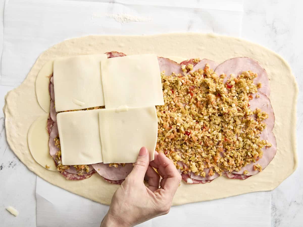 Die letzte Käseschicht zu einer Muffaletta-Rolle hinzufügen