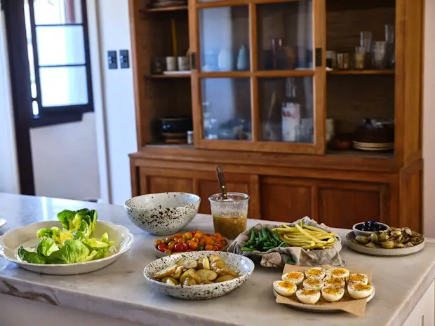 Zutaten für eine Nicoise auf einer Kücheninsel angeordnet, darunter hartgekochte Eier, grüne Bohnen, Kartoffeln, Oliven, Salat