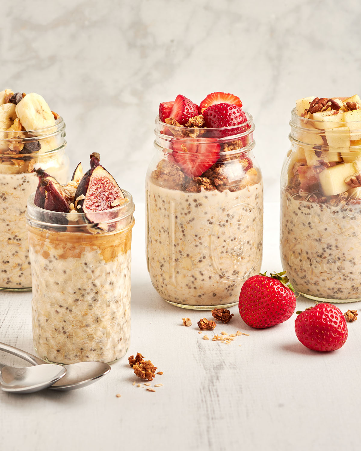 4 Gläser Overnight Oats, garniert mit verschiedenen frischen Früchten und Granola