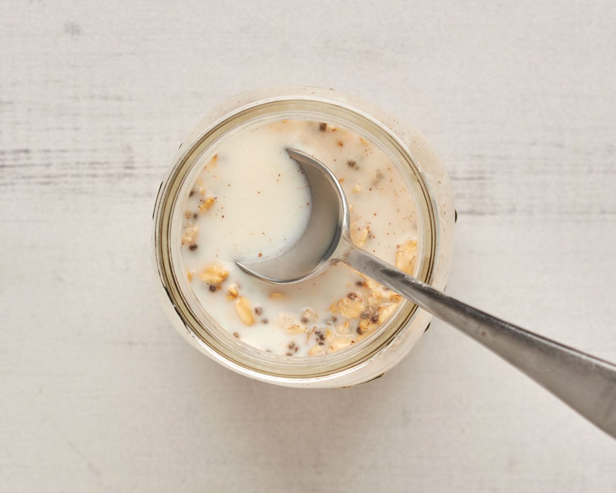 Löffel in Overnight Oat Gläser mit einem Schuss Milch auf dem Löffel