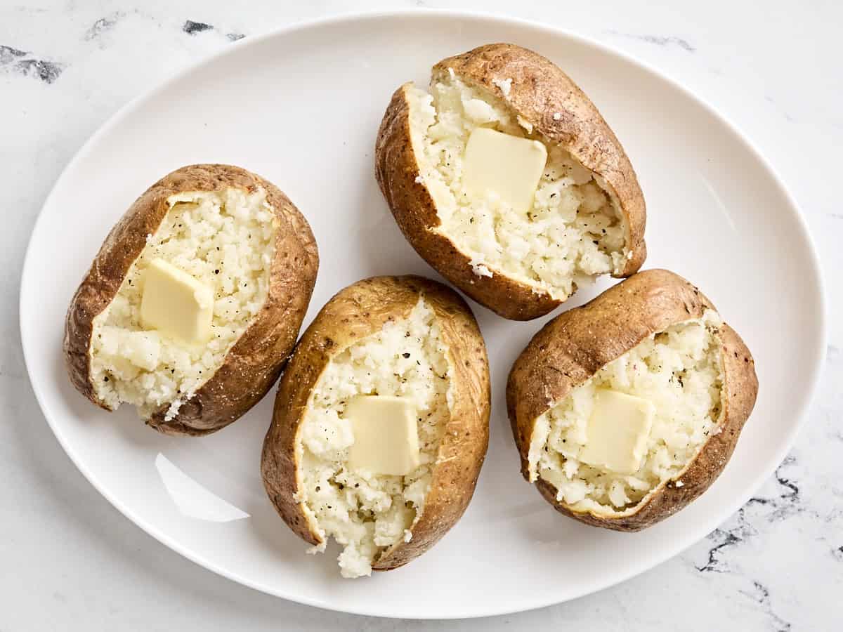 Vier aufgeschnittene, in der Heißluftfritteuse gebackene Kartoffeln mit Butter obendrauf.