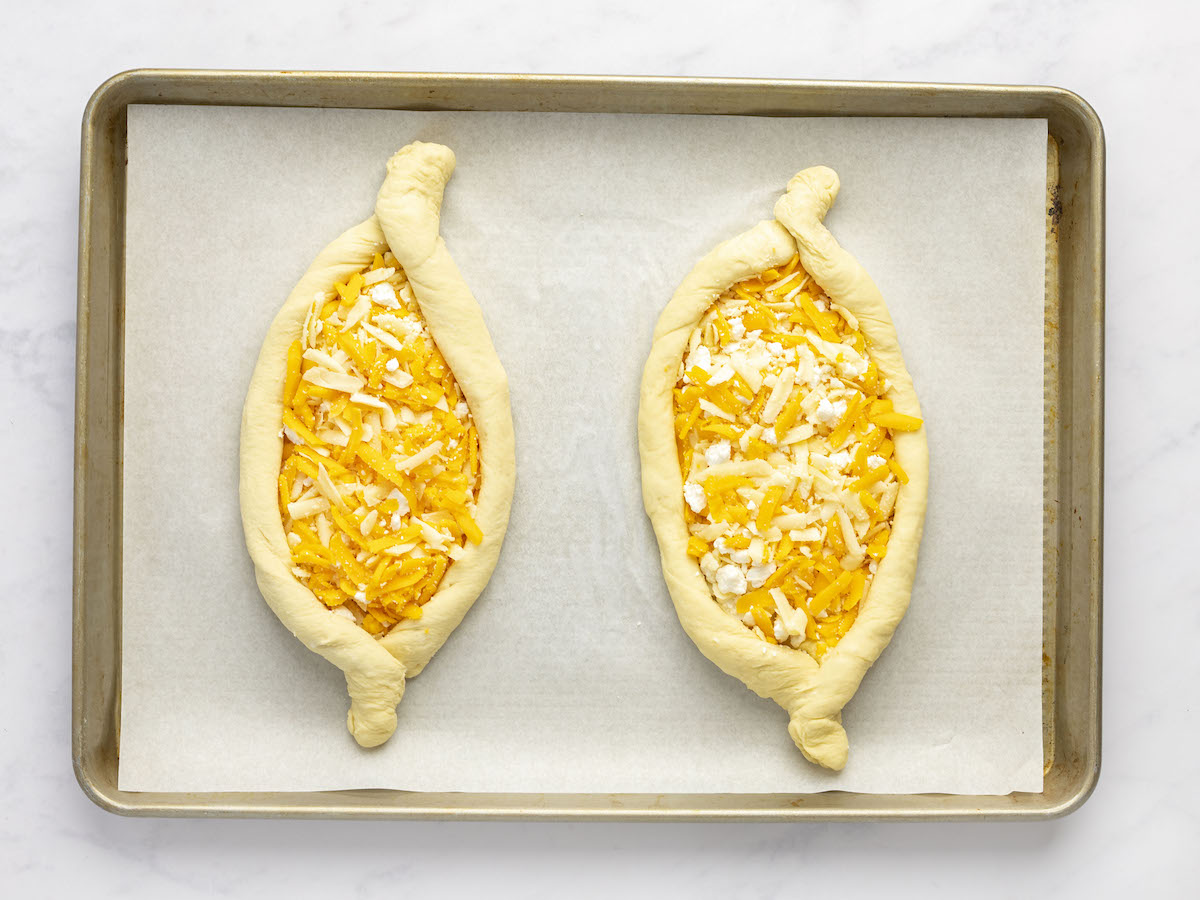 zwei mit Käse gefüllte Chatschpuri auf einem mit Backpapier ausgelegten Backblech