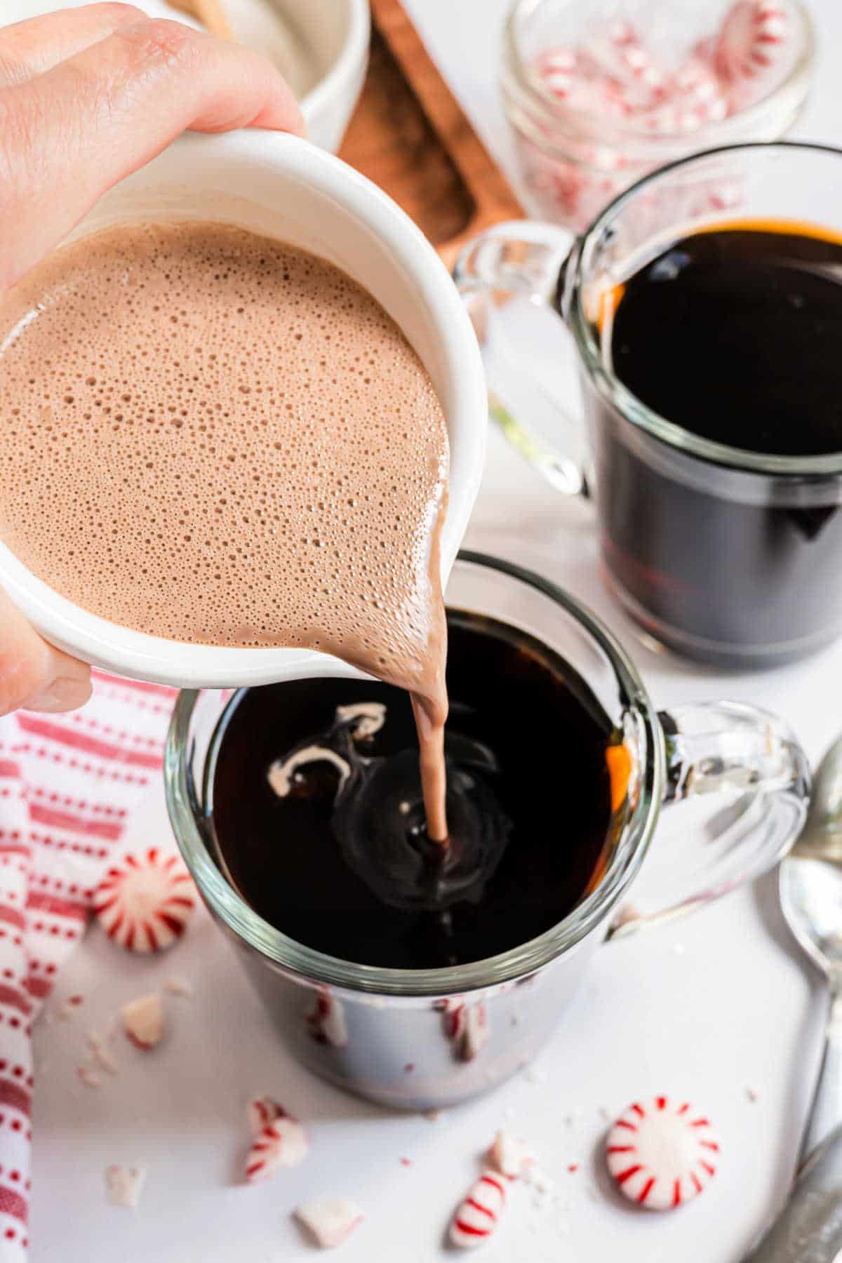 Selbstgemachter Milchkännchen wird in eine Tasse heißen Kakao gegossen.