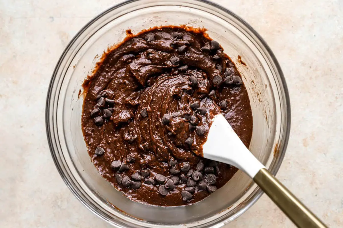 Brownie-Teig mit Schokostückchen in einer Glasschüssel mit einem Gummispatel.