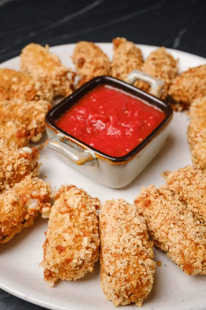 A plate of extra crispy homemade mozzarella sticks served around a delicious dipping sauce.