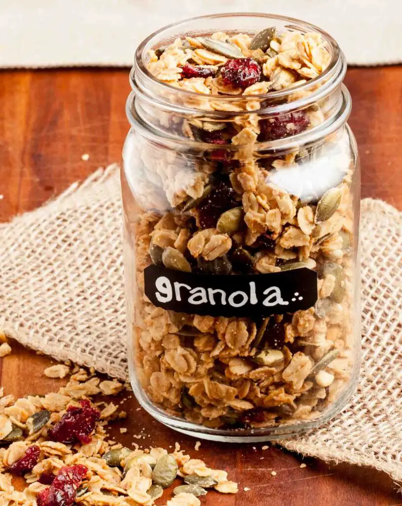 A glass jar filled with homemade crunchy granola, placed on a burlap cloth.