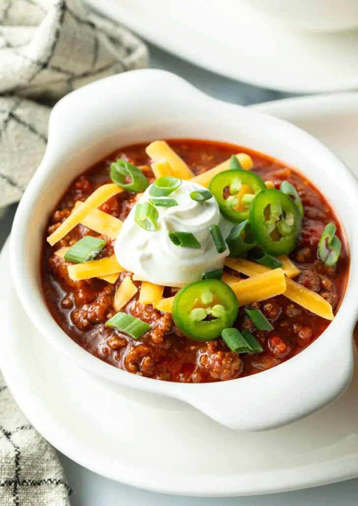 Draufsicht auf eine weiße Schüssel bohnenloses Chili, garniert mit geriebenem Käse, Jalapeño-Scheiben, Sauerrahm und gehackten Frühlingszwiebeln.