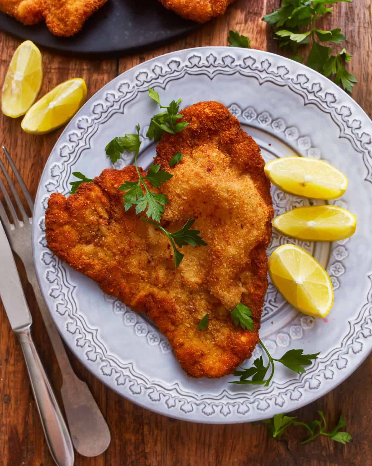 Blick von oben auf eine Portion Schweineschnitzel auf einem Teller mit Zitronenspalten.