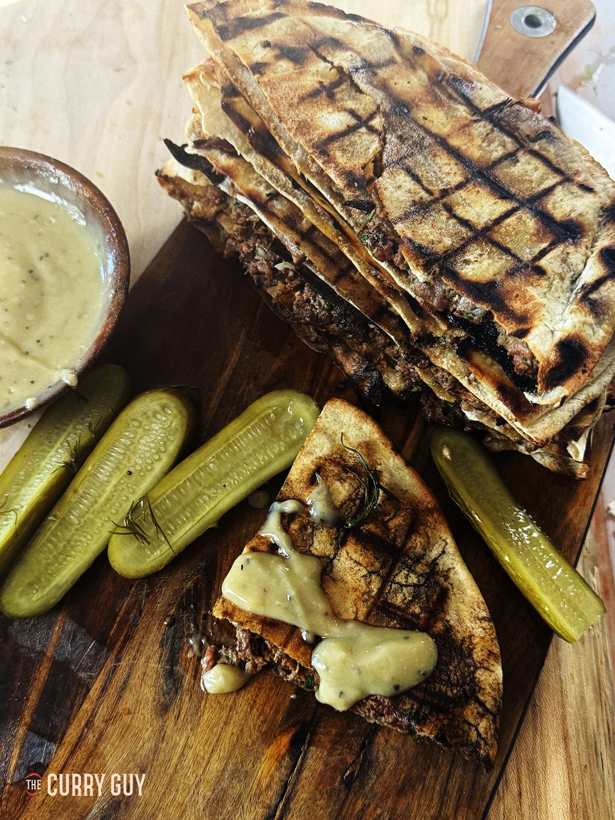 Mit Fleisch gefüllte Pitas (Areyes) auf einer Servierplatte mit Gurken und Tahinisauce.