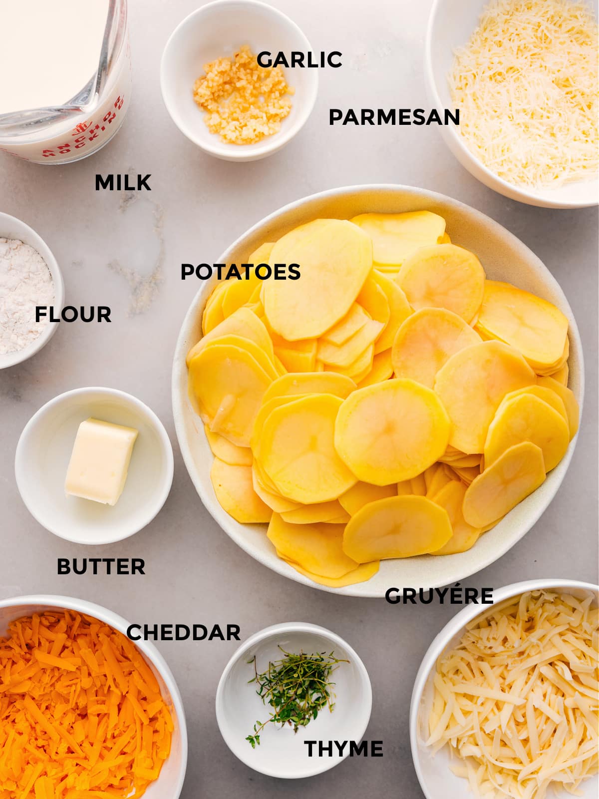 Die Zutaten für dieses Rezept – Kartoffeln, Mehl, Butter, Thymian, Käse, Milch und Knoblauch – sind vorbereitet und können einfach zubereitet werden.